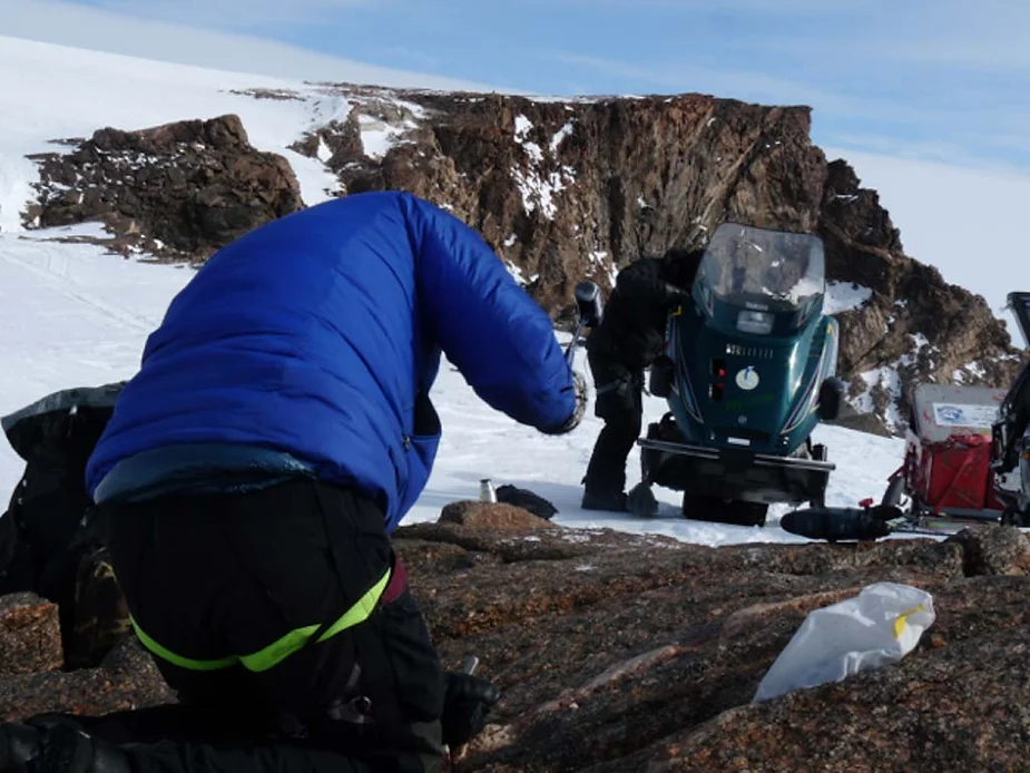 Bent over, gathering samples.